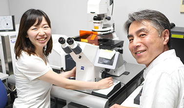顕微鏡の前で笑顔で写真に写る石龍悠さんと男性